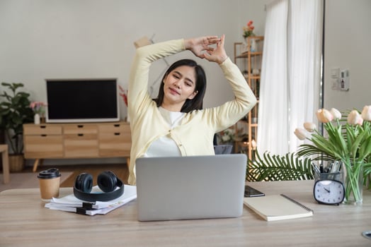 Young woman stretching at her desk in a home office, promoting wellness and relaxation during work. photo