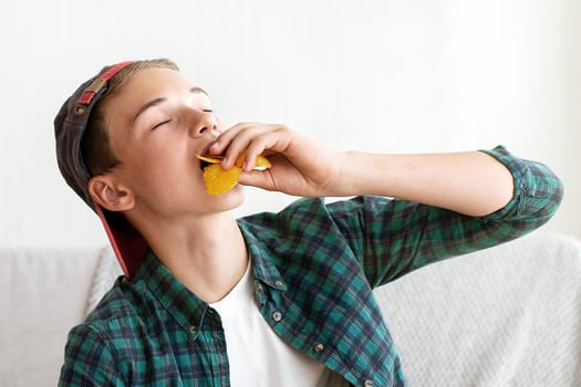 Teen guy enjoying chips while watching football game on TV at home, copy space photo