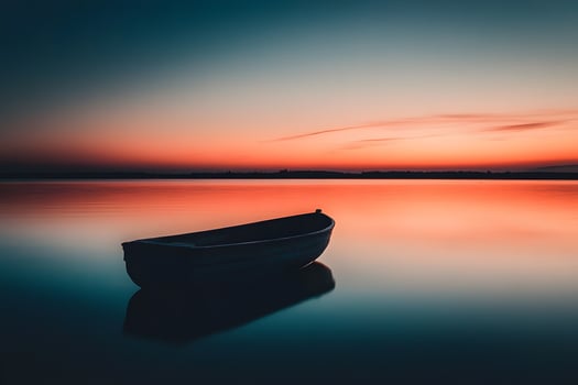 Boat silhouette on the horizon with a sky filled with warm orange and pink hues at sunset photo
