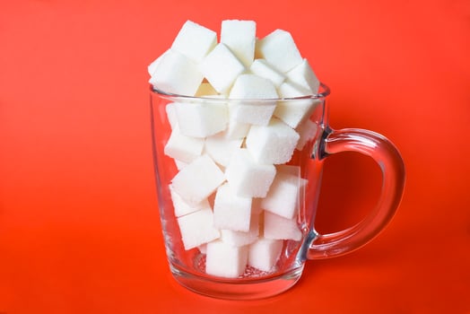 Transparent mug full of refined white sugar cubes on red background photo