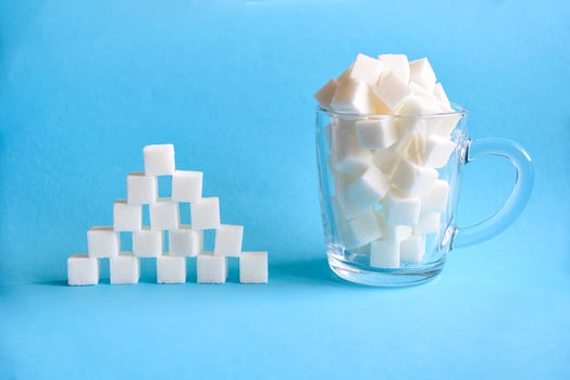 Transparent mug full of refined white sugar cubes and pyramid made from cubes of white sugar on blue background. Copy space photo