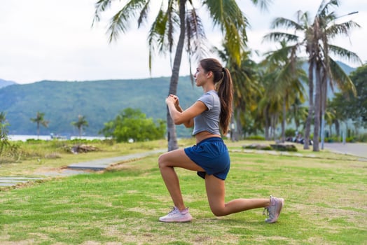 Young slim woman squatting and doing sport exercise against sunset and beach with palms photo