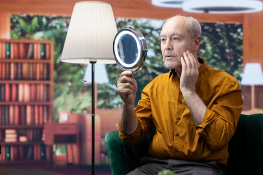 Elderly man applying serum and moisturizing cream on his cheeks, pampering skincare daily routine to preserve aging skin. Person using rejuvenating lotion for grooming, personal care. photo