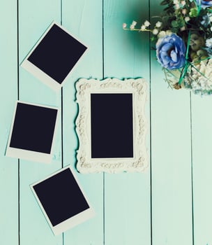 Decorative empty photo frame and blank polaroids on a teal wooden surface with a bouquet of flowers