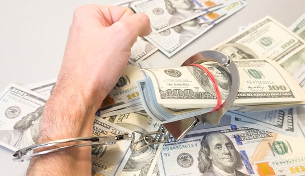 Folded hands and handcuffed hands resting on a table in front of money. photo
