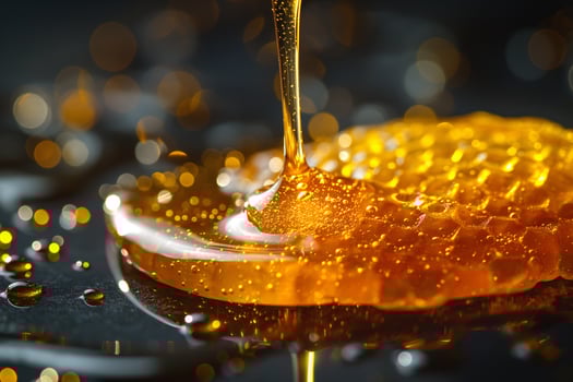 Golden honey drips from honeycomb creating a sweet glistening pool on a dark surface. photo