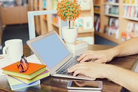 Person typing on a laptop at a cozy cafe with books and a coffee cup nearby photo