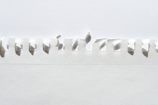 Close-up of torn white paper with perforated edge and folded tabs against light background. photo