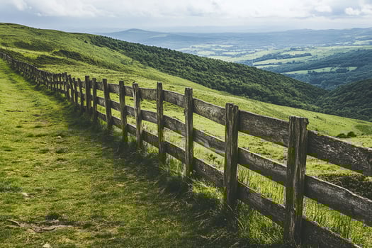 Rustic Wooden Fence with Rolling Green Hills and Forested Landscape under Cloudy Sky photo