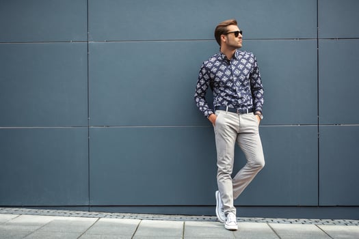 A man in sunglasses and a shirt leaning against a wall photo