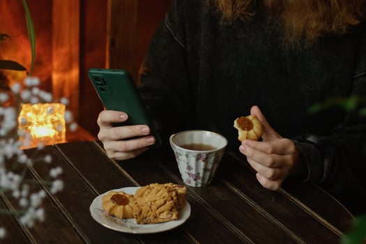 Tea time, daily routine. Woman using mobile phone sitting at table with cup of tea and pastries in cozy room. photo