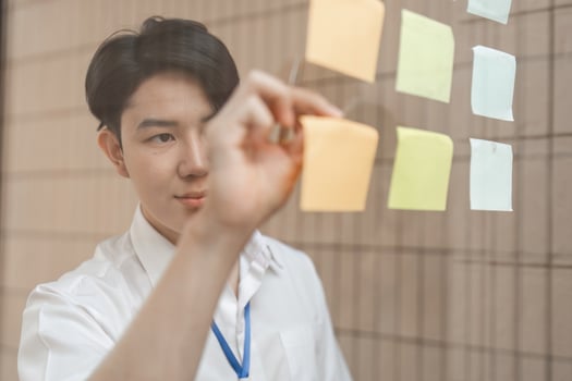 Young professional arranging sticky notes on glass wall, organizing ideas and enhancing workflow in modern office. photo