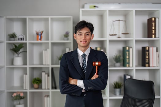 Confident young Asian lawyer standing with arms crossed in office, holding gavel, representing law practice. photo
