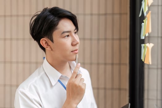 Young professional contemplating sticky notes on glass wall, strategizing tasks and improving workflow in modern office. photo