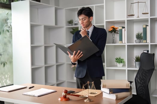 Thoughtful young Asian lawyer analyzing case files and legal documents in modern office setting. photo