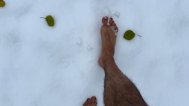 Top view of male bare feet stepping on white snow. Legs of man going on snowy trail. Young guy hardening at cold winter. Concept of healthy lifestyle. POV Slow motion photo