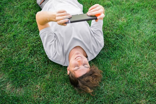 Young man smiling confident playing game at park lying on a grass. Technology and gaming concept photo