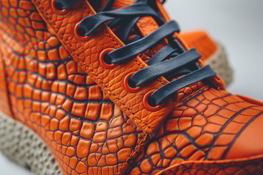 Close-up of stylish orange crocodile-patterned sneakers with black laces and textured soles. photo