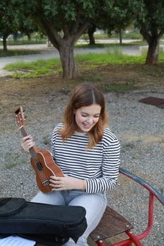 Girl Puts The Musical Instrument Ukulele In The Case Outdoor In Park photo