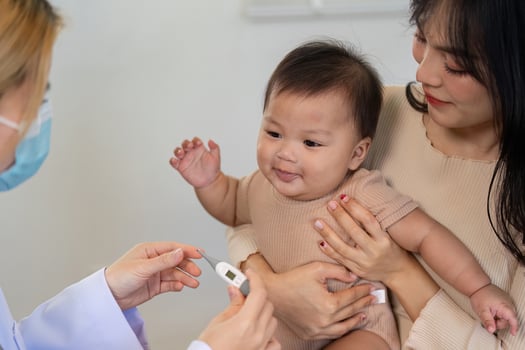 Pediatric doctor checking baby temperature while parent holds child in clinic. photo