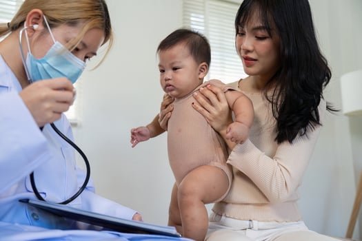 Pediatric doctor using stethoscope to examine baby while parent holds child in clinic. photo