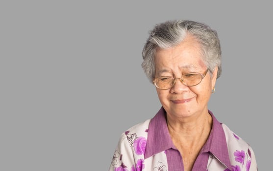 Beautiful elderly Asian woman looks down with a smile while standing on a gray background photo