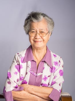 Beautiful an elderly Asian woman looking at the camera with a smile while standing on a gray background photo