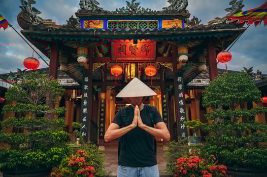 male tourist in a Vietnamese Non La hat prays at temple on a Buddhist pagoda in Hoi An in Vietnam in Asia photo