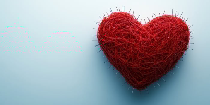 Red heart made of thread with pins on a light blue background depicting love and creativity photo