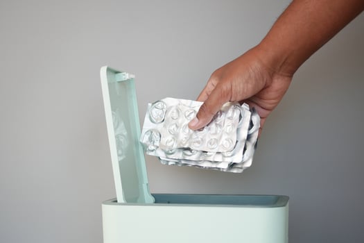 Person disposing of used medical blister packs in a trash bin photo