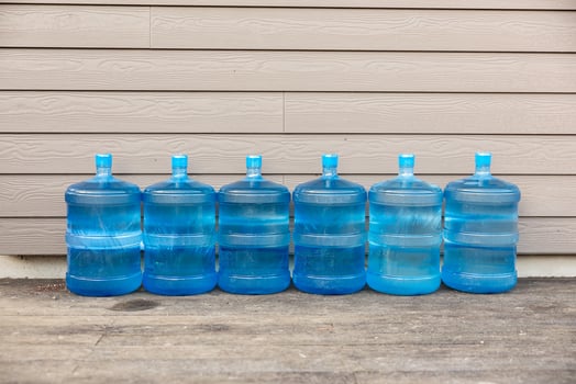 Six Blue Water Jugs on Wooden Surface Against Beige Paneled Wall photo