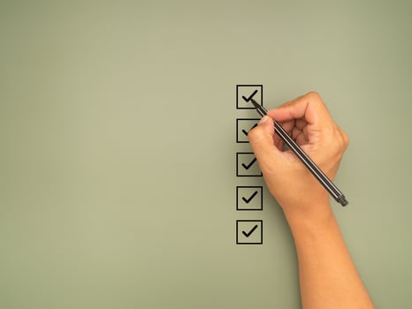 Hand holding a pen check-marking on the checklist box on a green background photo