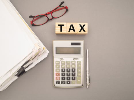 Stack of documents with binder clips, glasses, calculator, and Wooden cubes with the letters TAX on a gray background photo