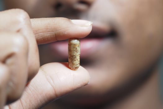 Person holding a capsule close to their mouth in natural light photo