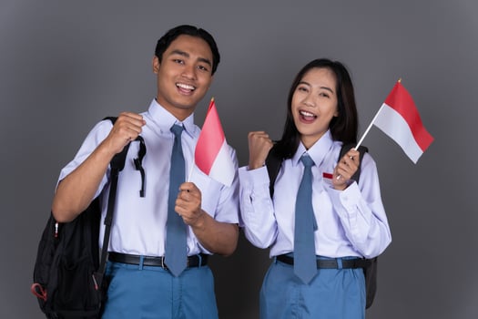Indonesian Male and Female High School Student in Uniform Waving Indonesian Flag Isolated Background photo