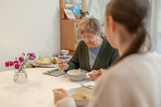 Senior woman enjoying meal with young woman at home. Concept of family bonding, aging, and healthy eating. Grandmother spending quality time with granddaugther at home. photo