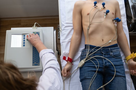 A female doctor performs an ECG on a young man in a hospital room, carefully monitoring his heart health during a routine checkup. photo