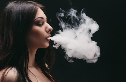 Brunette woman vaping electronic cigarette with smoke on black background closeup. Young woman smoking e-cigarette to quit tobacco. Vapor and alternative nicotine free smoking concept, copy space photo