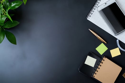 Dark desk with phone, notepad, pen, plant, sticky notes. photo