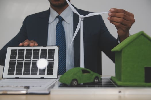 Man holding a laptop and a wind turbine in front of a green house and a car photo