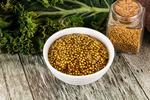 A bowl of mustard next to a bowl of mustard seeds photo
