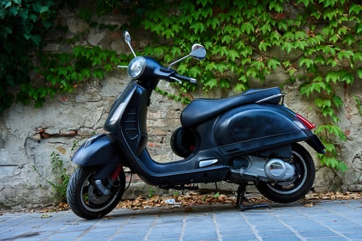 Black scooter parked on cobblestone street against old brick wall covered in green ivy. Vintage urban transportation photo