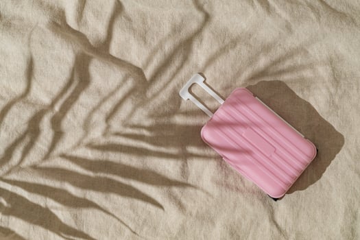 Summer day scene with tropical palm tree leaf shadow and pastel pink baggage on sand color linen background. Minimal stylish travel concept. Trendy summertime adventure idea. Flat lay, top view. photo