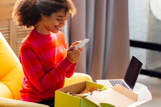 A young attractive African woman in casual clothing is unpacking a beauty box with cosmetic products. A charming black girl is smiling and holding face cream. photo
