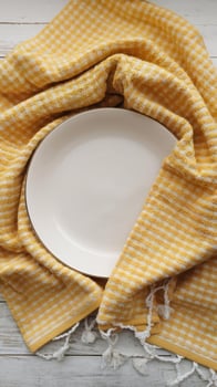 Yellow gingham towel with white plate on wooden table photo
