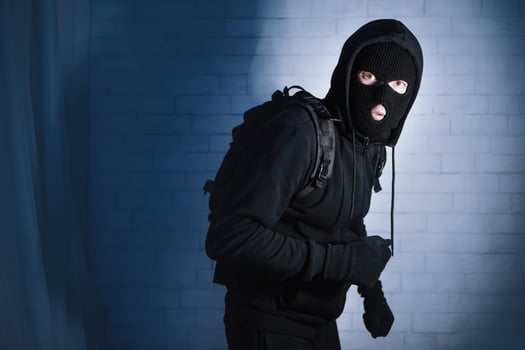 Burglary Concept. Intruder in black balaclava standing in apartment or office in the dark, looking at camera photo