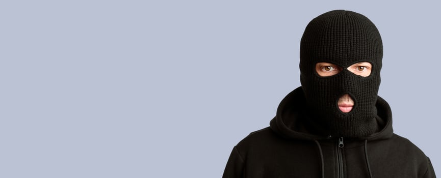 Closeup headshot of criminal wearing black balaclava and hoodie looking at camera, copy space, isolated over white wall photo