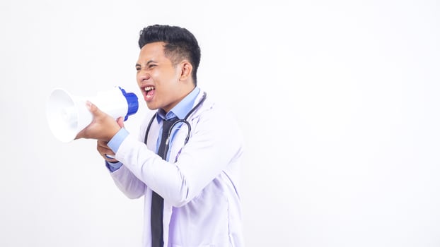 Frustrated Asian Male Doctor Shouting on Megaphone on White Background photo