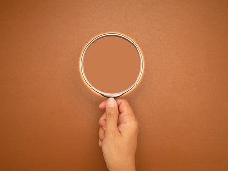 Magnifier in hand with a brown background photo