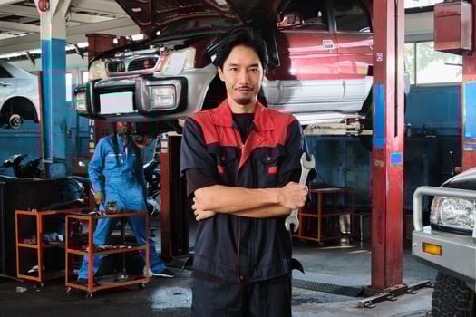 Asian male professional mechanic with wrench, arms crossed stands in car fix garage, serious maintenance service jobs, and machine engineer work in automotive transport industry station. photo